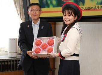ミス・フレッシュ秋田（右）から佐竹知事へ「かづの北限の桃」を贈呈の内容を表示