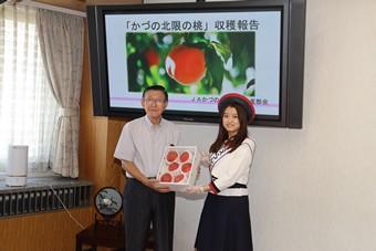 ミス・フレッシュ秋田（右）から佐竹知事へ「かづの北限の桃」を贈呈の内容を表示