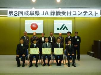 最優秀賞の髙井さん(前列中央)と優秀賞の塚本さん(前列中央左)と優良賞の萱野さん(前列中央右)担当者(前列)・審査員の方々(後列)の内容を表示