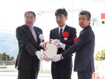 関係者らによる施設引渡し（左から小林組合長、梶田副本部長、川崎社長）の内容を表示