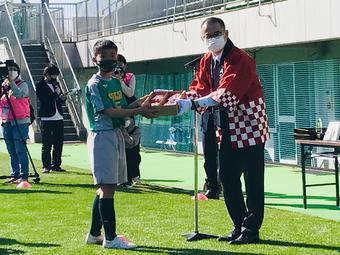 優勝したFC.フェルボール愛知の選手(左)へ「美濃娘」を贈る中島部長(右)の内容を表示