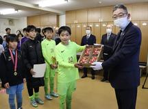 優勝したFCガウーショの選手（左）へ「美濃娘」を贈る藤塚副本部長（右）の内容を表示
