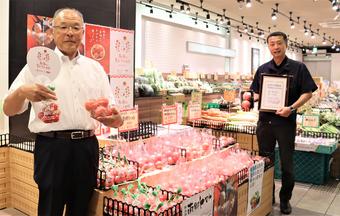 夏トマトの日をPRする西村県本部長(左)と藤井社長の内容を表示