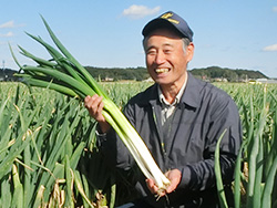 自慢のいなしきねぎを手に満面の笑顔のJA稲敷 ねぎ部会部会長の平山 迪雄さん