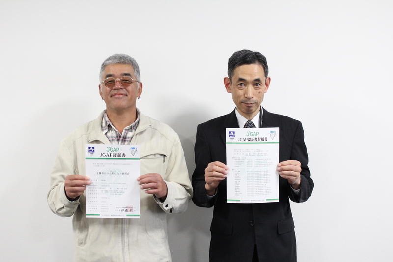 認証書を掲げる草野会長(㊧)と事務局の中村審査役(㊨)の内容を表示