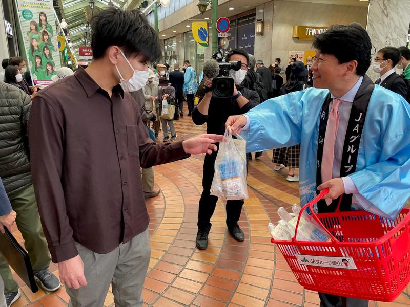 伊原木隆太県知事から「きぬむすめ「にこまる」を受け取る商店街利用者の内容を表示