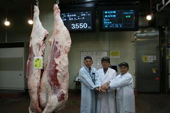 「金賞」に輝いた肉牛を前に記念撮影。落札した小島精肉店（左）、猪股氏（中央）、梶原実行委員会会長（右）の内容を表示